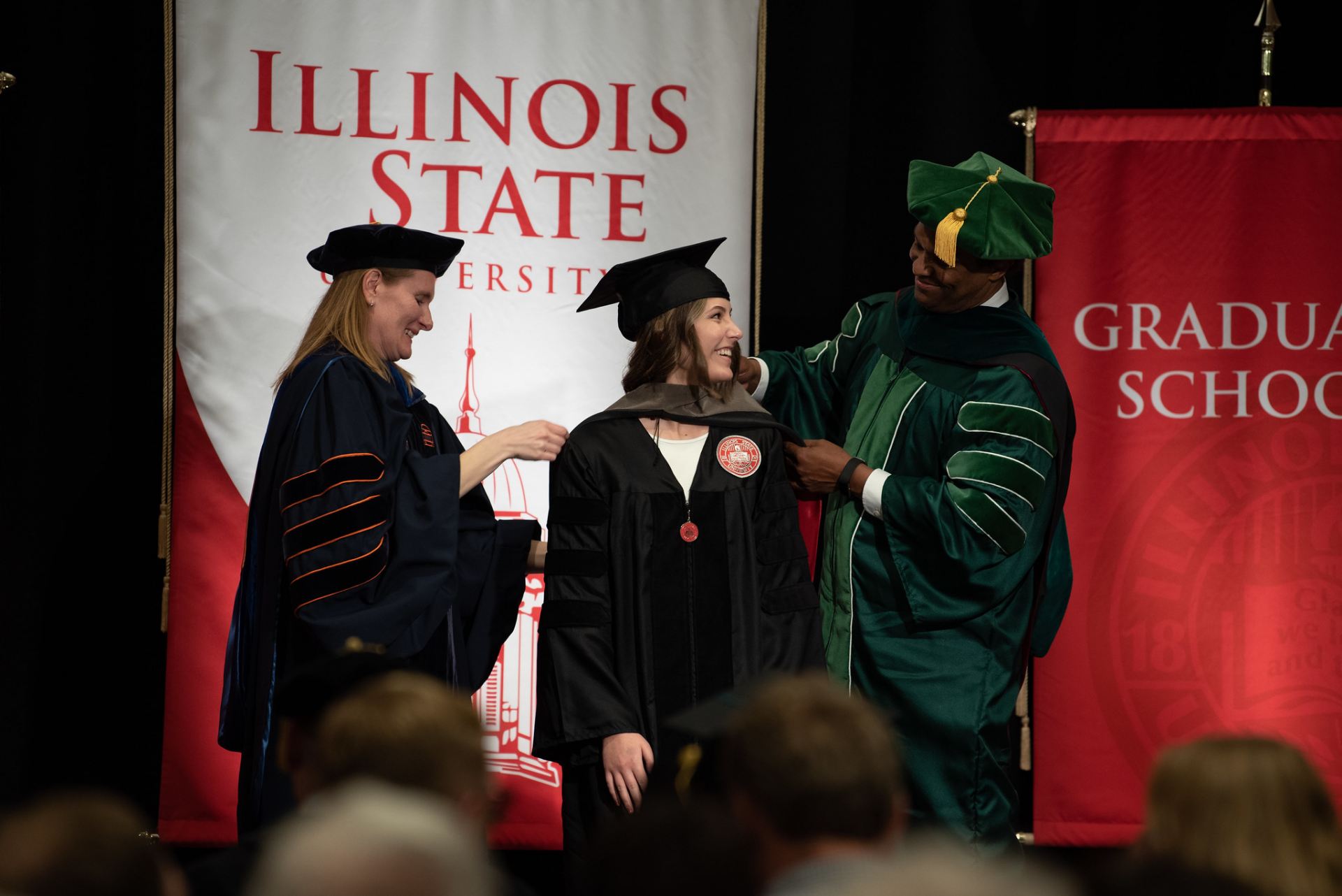 Two people putting a sash on a graduate on stage.