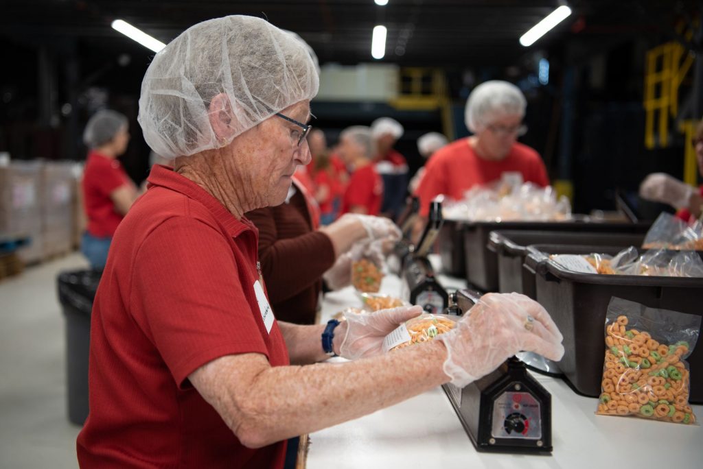 A woman wearing a hairnet seals a bag of cereal.