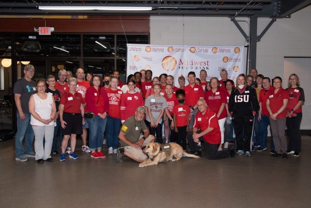 Group photo of people and one service dog in front of a Midwest Food Bank banner.
