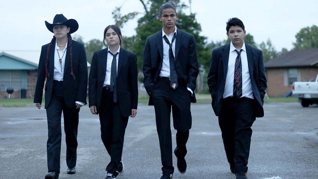 Cuatro adolescentes con traje y corbata caminando 