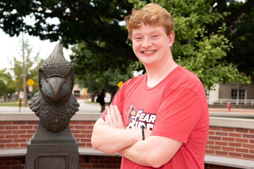 student posed with redbird bust on quad