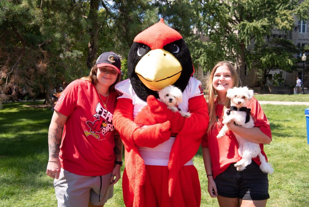 Two students and their dogs pose with Reggie Redbird