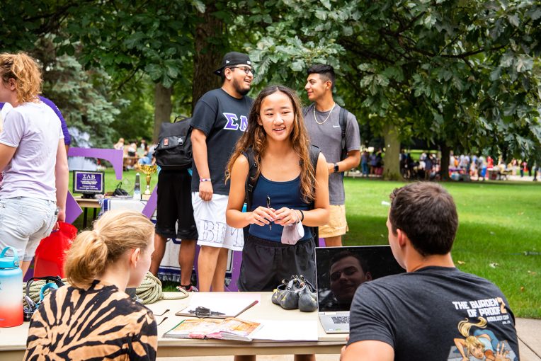 person standing and speaking to another person sitting at a table on the Quad