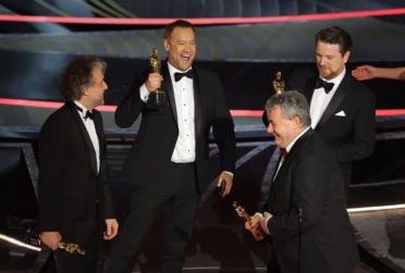 Four men in tuxedos standing on stage and smiling holding Oscars
