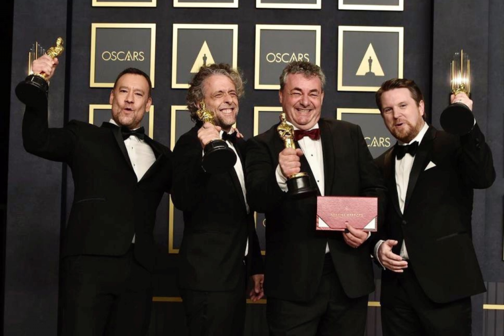 Four men standing and smiling holding Oscar awards