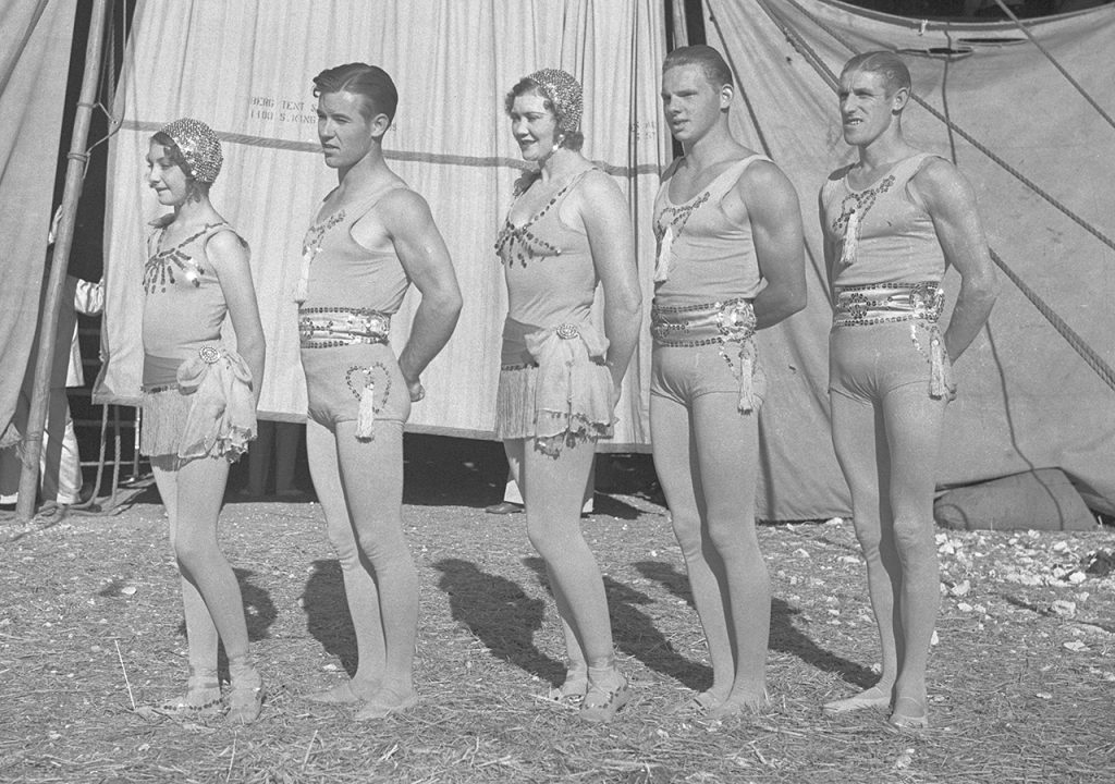 Image of five aerialists in wardrobe standing in front of a circus tent.