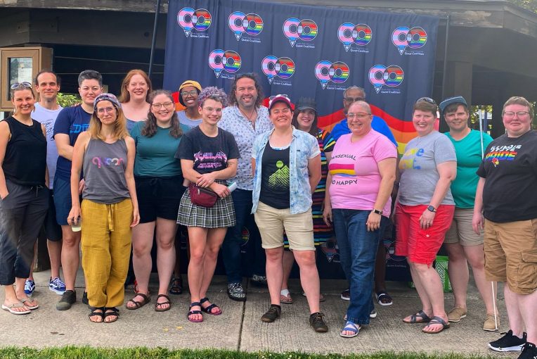 A crowd of Queer Coalition members stand in front of a picnic shelter