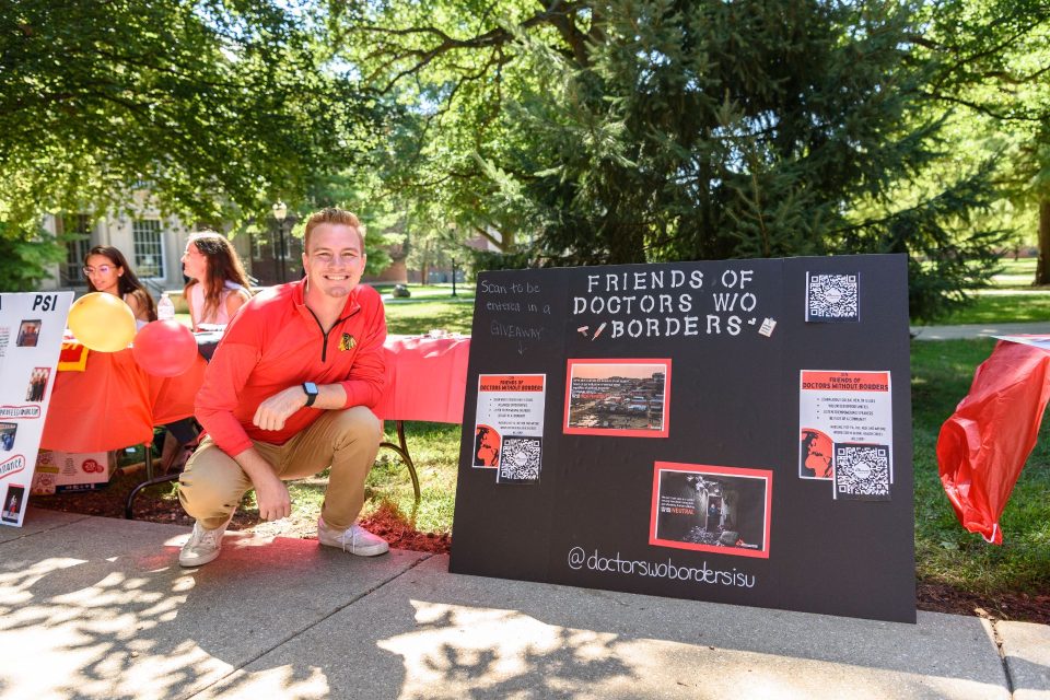 student squats next to the poster board at the Friends of Doctors Without Borders table at Festival ISU