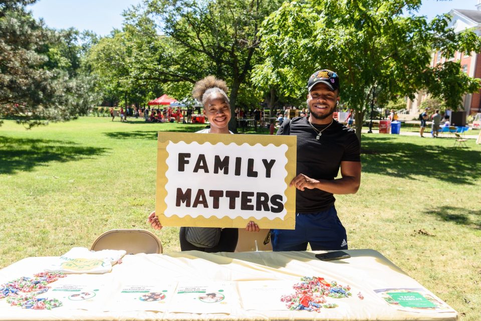 Two students hold up a sign that says "Family Matters" at their RSO's table at Festival ISU