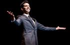 Michael Carbonaro wearing a suit on stage with his arms extended