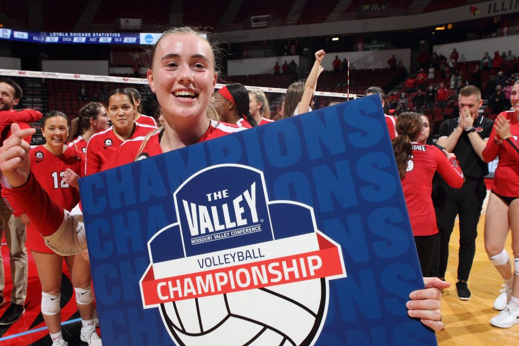 Illinois State volleyball player smiling, holding a blue sign that reads: "The Valley volleyball championship."