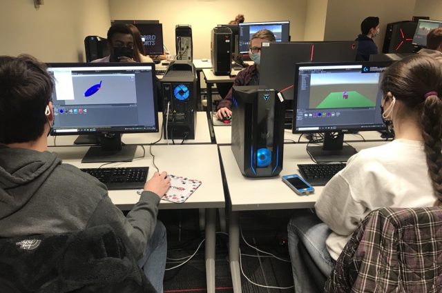 A group of masked students sit at a computer clump in Julian Hall working on their virtual reality (VR) projects on their computers