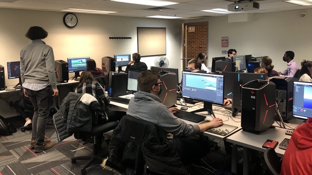 A group of students sit in a computer lab classroom with powerful machines that can handle the virtual reality tools they are working with