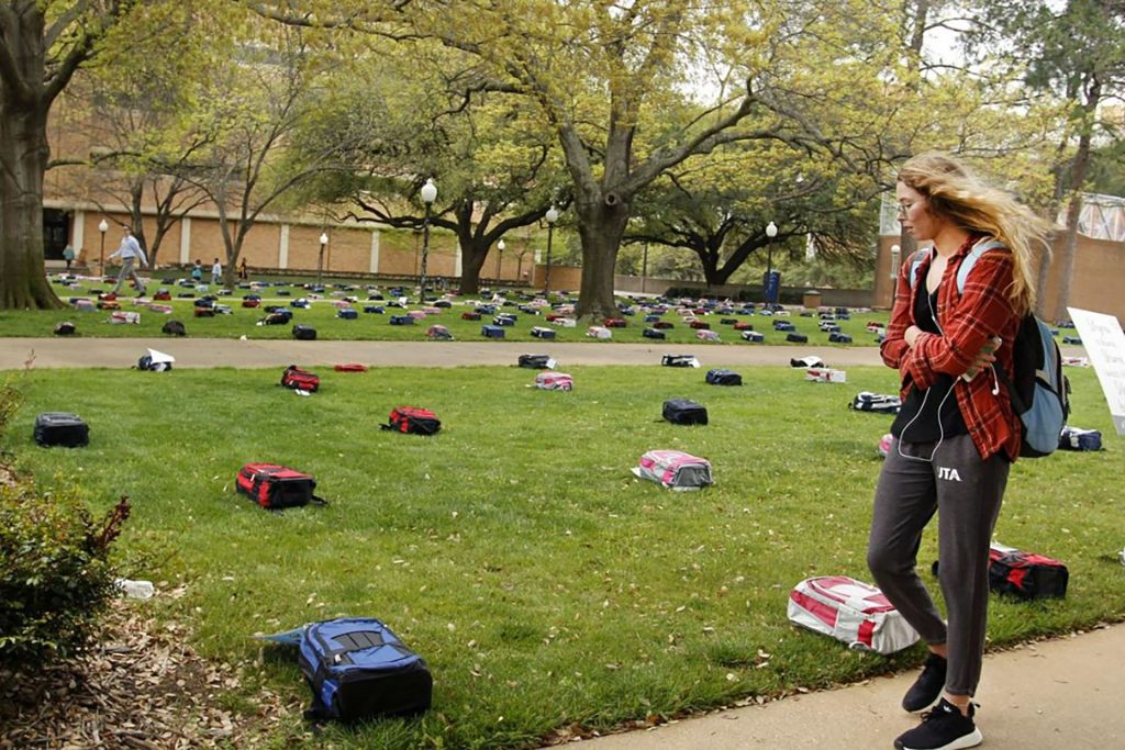 woman walking on a sidewalk looking at a bookbags place across a grassy lawn