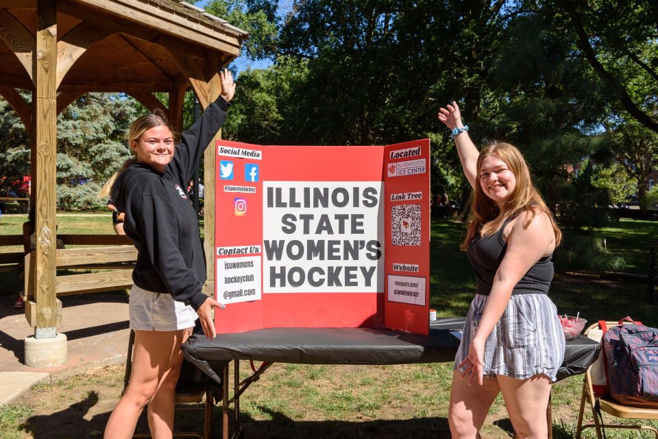 Two students gesture toward their poster board at their RSO's table at Festival ISU