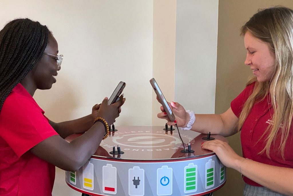 two students holding phones with their arms resting on a circular charging table