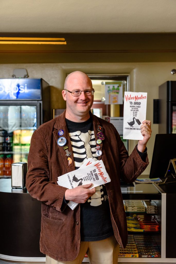 Dr. Eric Wesselmann holding paper pamphlets that say "Video Nasties" to promote his class.