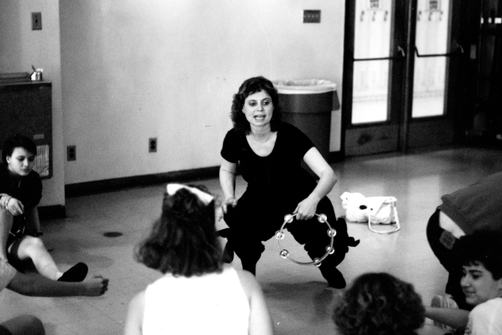 A woman holding a tambourine in a circle of students a