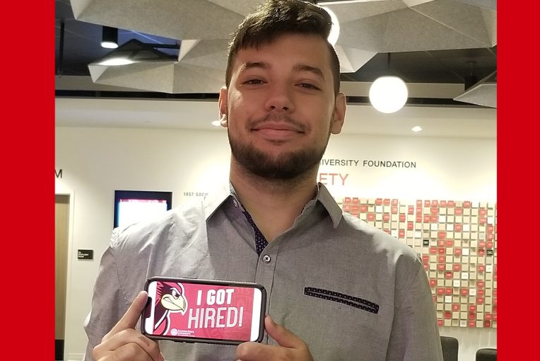 student holding a cell phone that reads "I Got Hired"