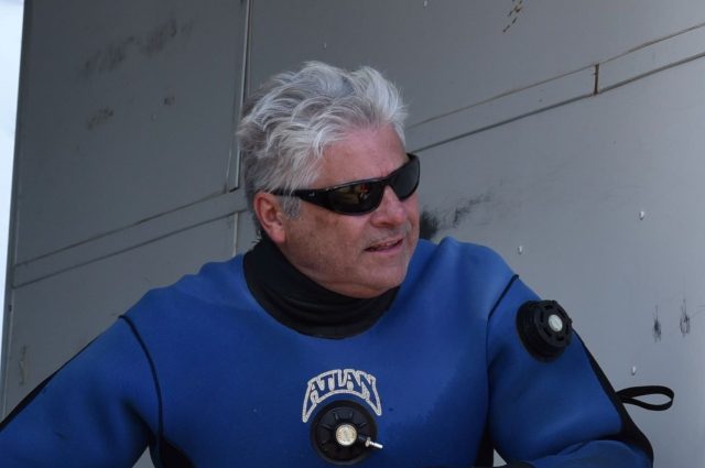 Gray haired man in sun glasses and a blue diving suit