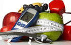 Photo of fruit, a blood glucose reader, a stethescope, and weights with a tape measure wrapped around.