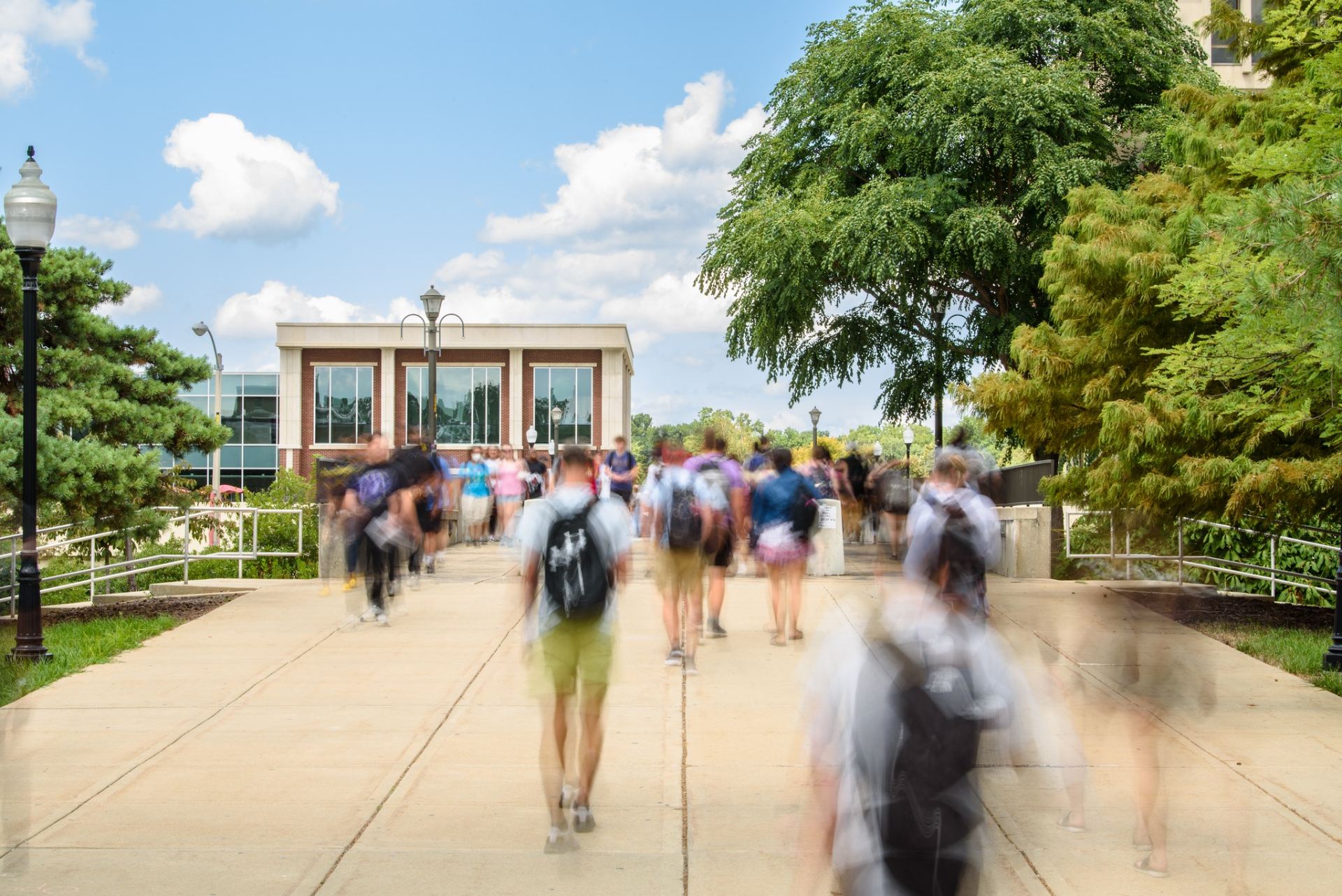 Blurred image of students walking on the College Avenue Bridge with the Bone Student Center in the background