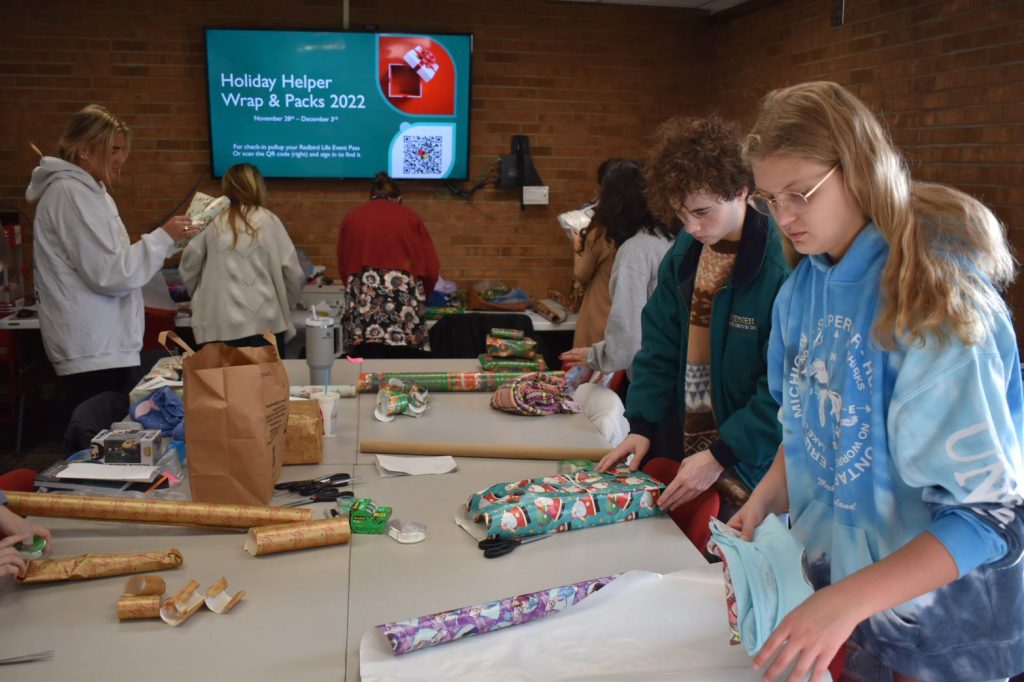 A line of volunteers wrap gifts at a table