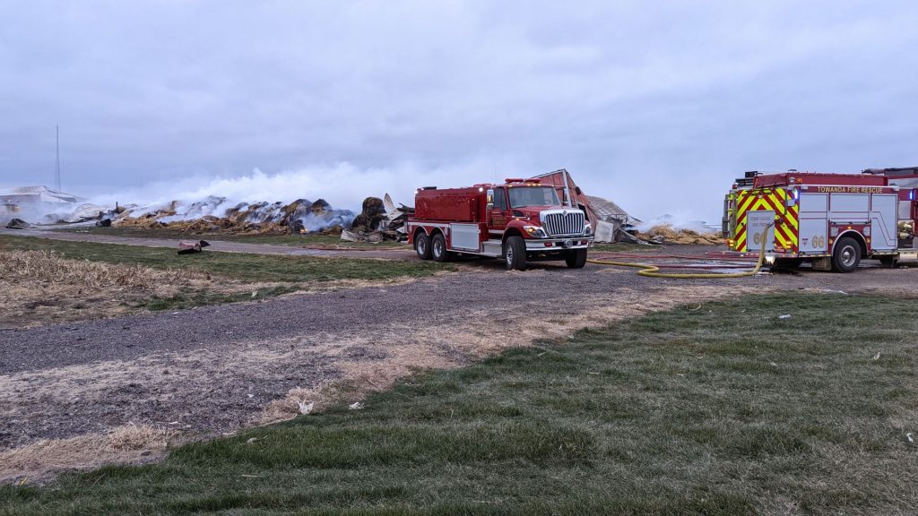 Fire trucks with smoldering debris in the background after a fire at ISU Farm.