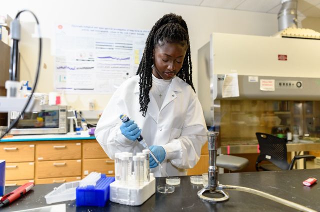Erinda Aidoo wearing a white lab coat uses a pipet