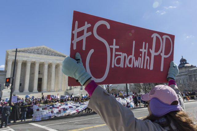 A person holding a pink "#StandwithPP" sign in front of the U.S. Supreme Court