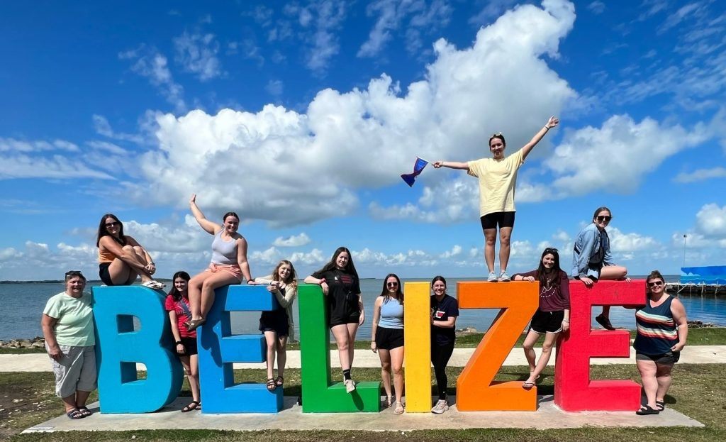 Students pose next to a sign for Belize