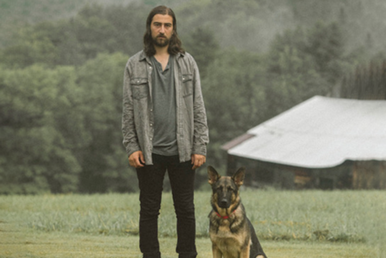 Noah Kahan standing in a field next to a dog