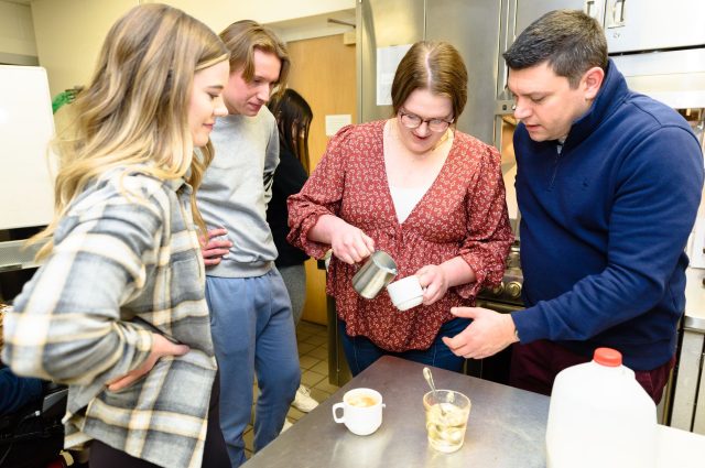 Two students and Dr. Erol Sozen observe as another student pours frothed milk into a latte.