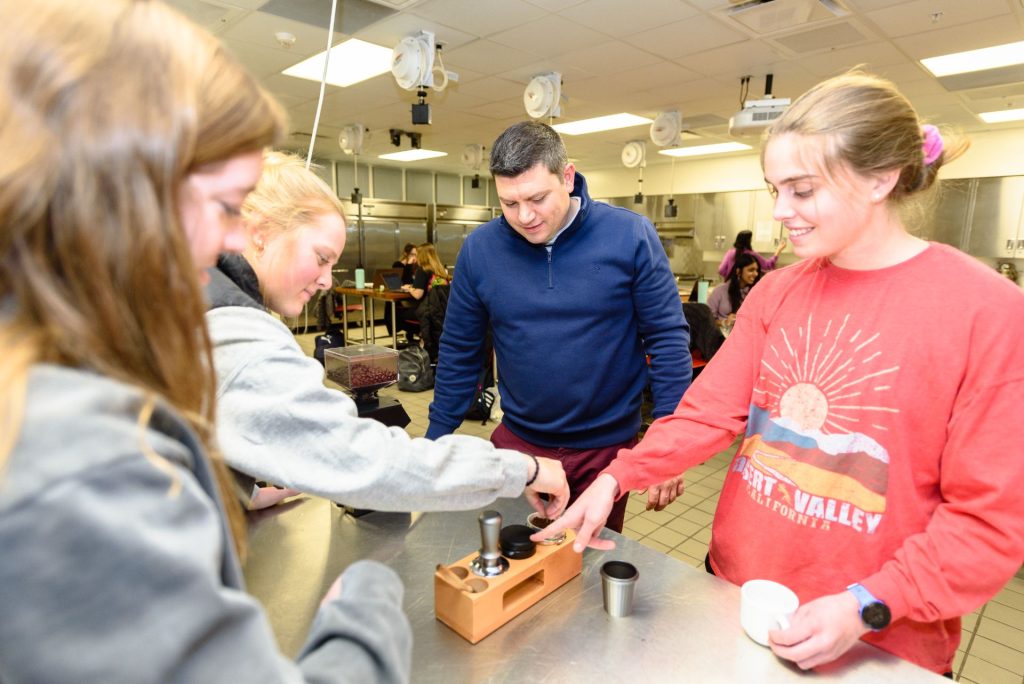 Three students take turns tamping coffee grounds as Dr. Erol Sozen observes and provides guidance