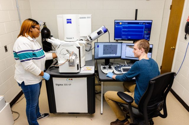 two students working in a lab with a large microscope