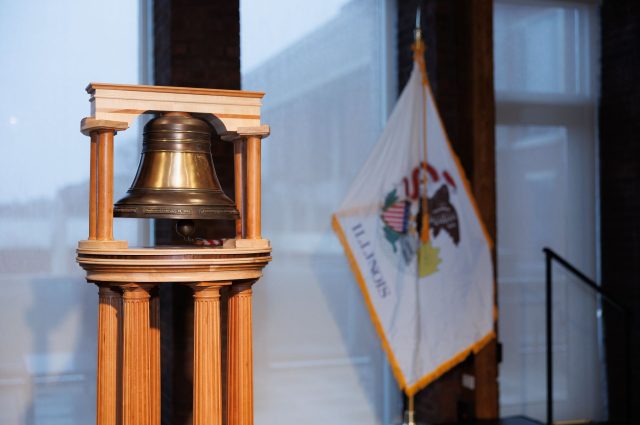 a bell on a stand with Illinois state flag in background