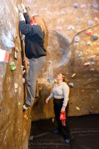 Student climbing on rock wall while being guided by another student on the ground