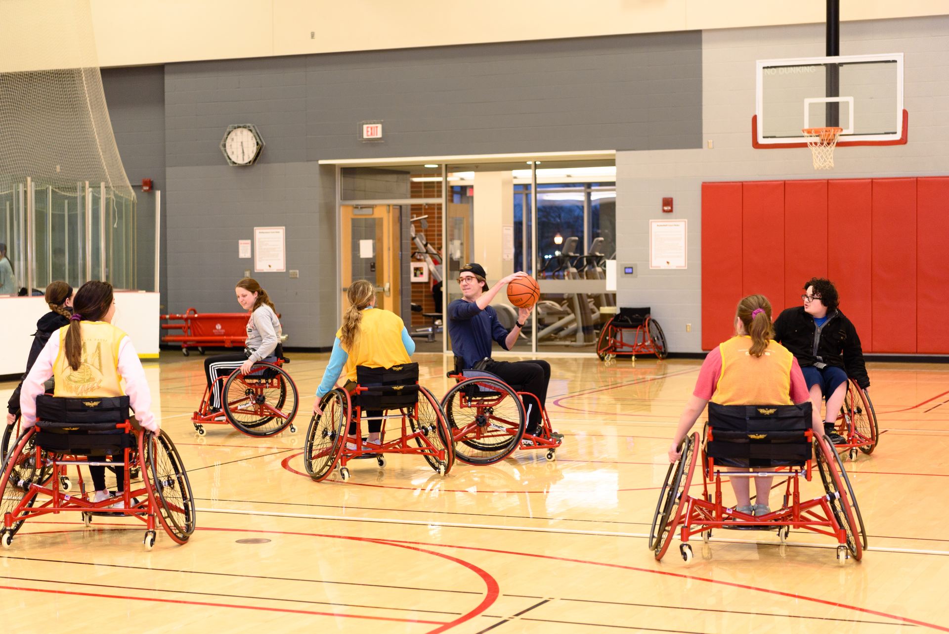A student in a wheelchair holds the basketball and looks for someone to pass to