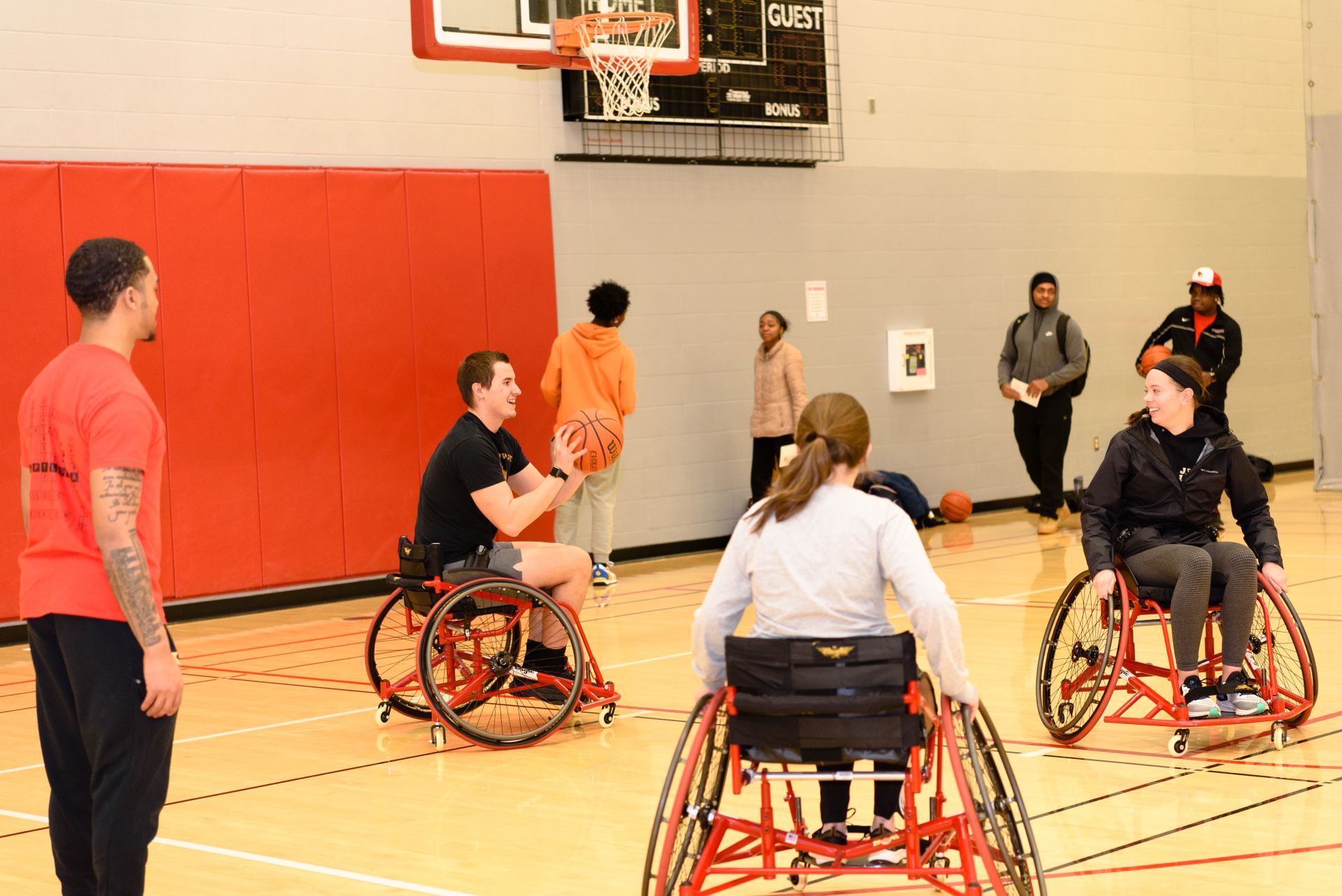 A student in a wheelchair at the end of the basketball court hold the ball while looking for a teammate to pass to