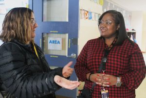     Dr. Christy Borders gestures with her hands while speaking with a smiling Chardon Hill-Hamilton in an elementary school hallway. 