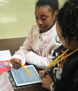 A girl and a young woman sit at a table working through fraction identification on an iPad. 