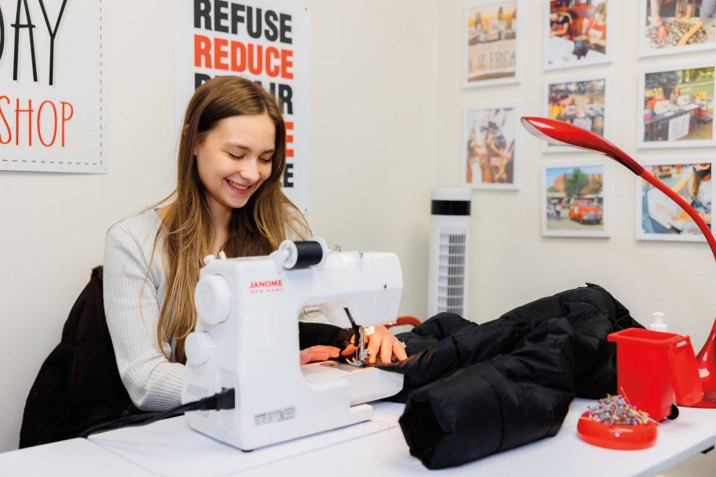 A student performs clothing repair while seated at a sewing machine