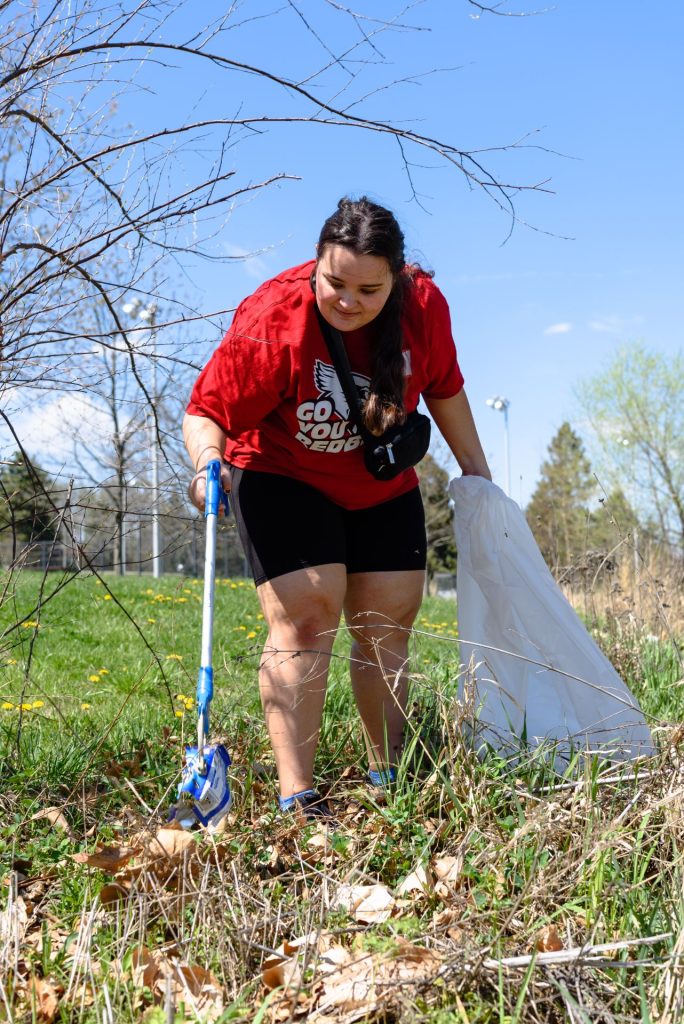 A student picks up a discarded chip bag using a trash picker while holding a large garbage bag.