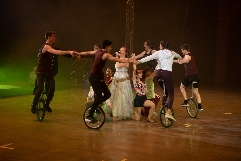 people on unicycles aurrounding a singer and dancers 