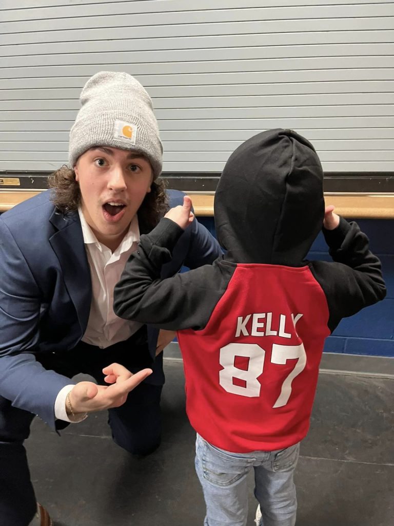 Wil points to Grayson sweatshirt which says "Kelly" and "87" on the back of it