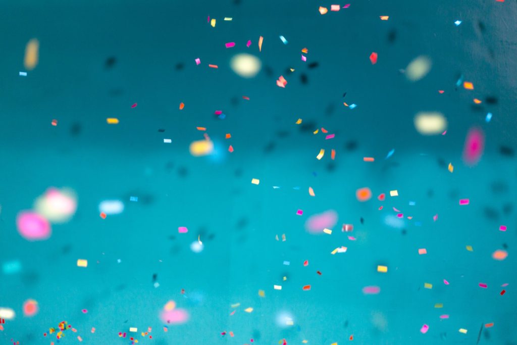 Teal background with a focus on multi-color confetti pieces in the foreground.