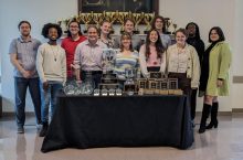 Group of students posed behind a table of trophies and awards