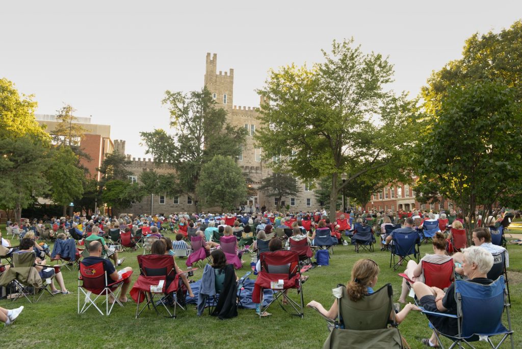 Dozens of people sitting in lawn chairs on the Quad listen to a concert