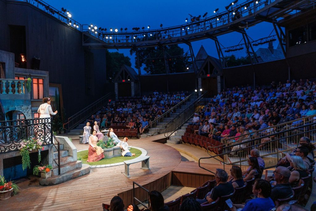 The Shakespeare Festival stage is illuminated with the audience in the background