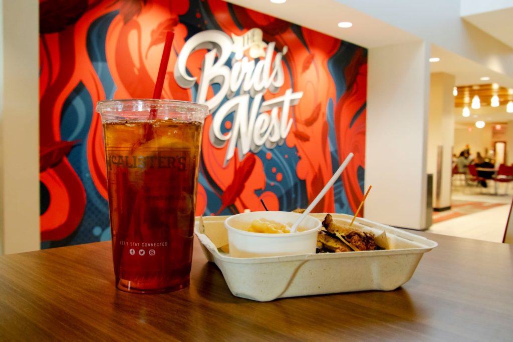 McAlister's iced tea sits on wooden table next to open to-go box with sandwich inside in front of Birds' Nest design.